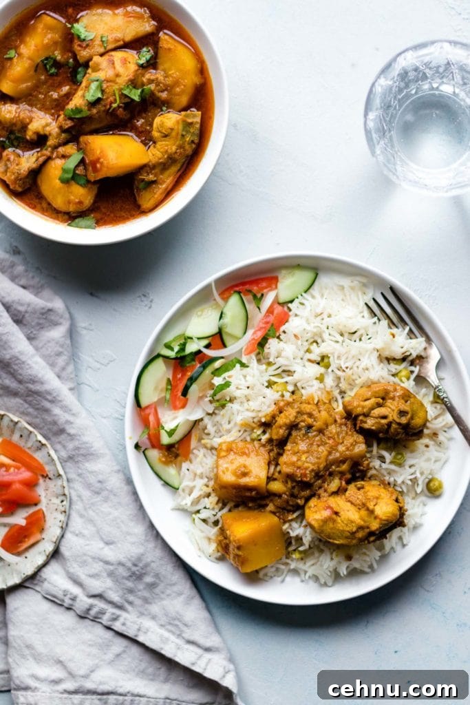 Chicken Curry with potatoes on a plate with rice and vegetables with a glass of water on the side