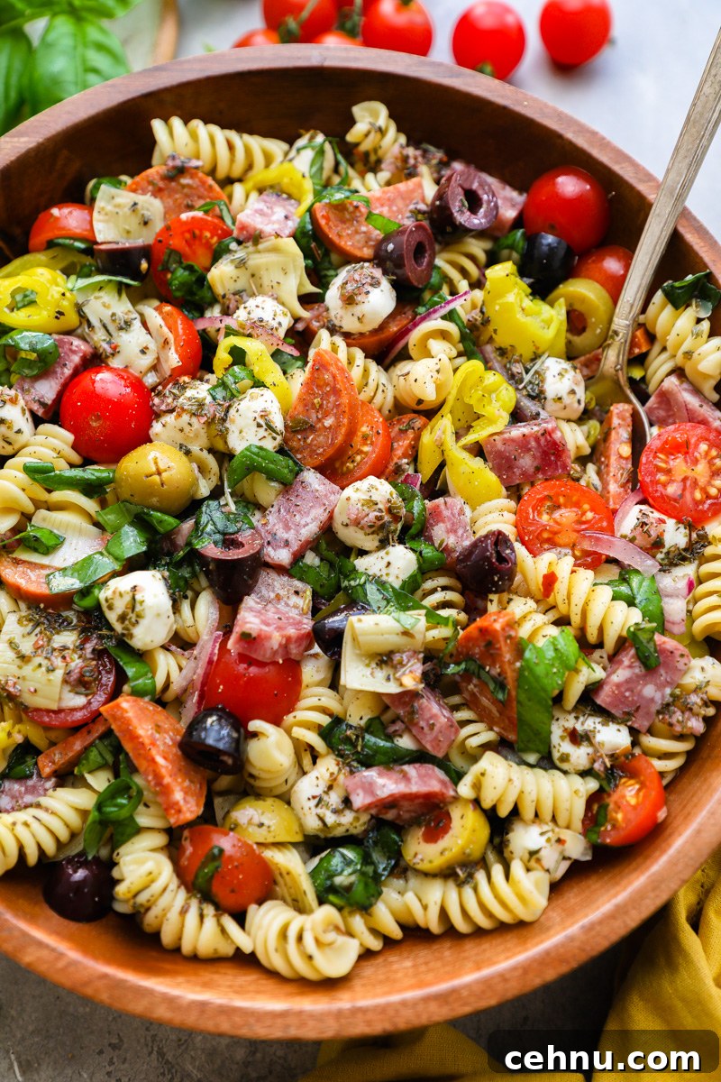 A serving bowl filled with Italian antipasto pasta salad surrounded by fresh cherry tomatoes and basil