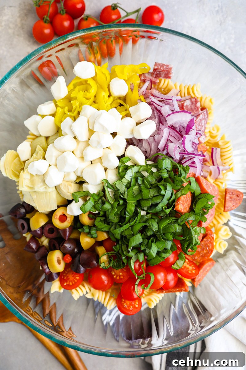 A large mixing bowl filled with ingredients used to make an antipasto pasta salad