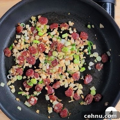 Chinese sausages and green parts of spring onion/scallion added to the pan