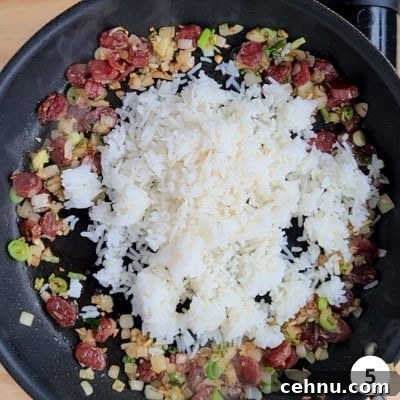 White rice poured into the centre of pan with sausages and onions pushed to the sides of pan