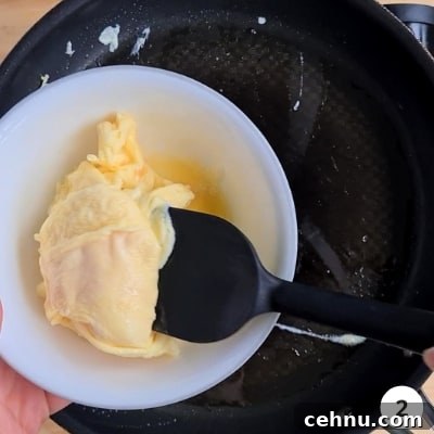 Scrambled eggs removed from hot pan, into a white bowl