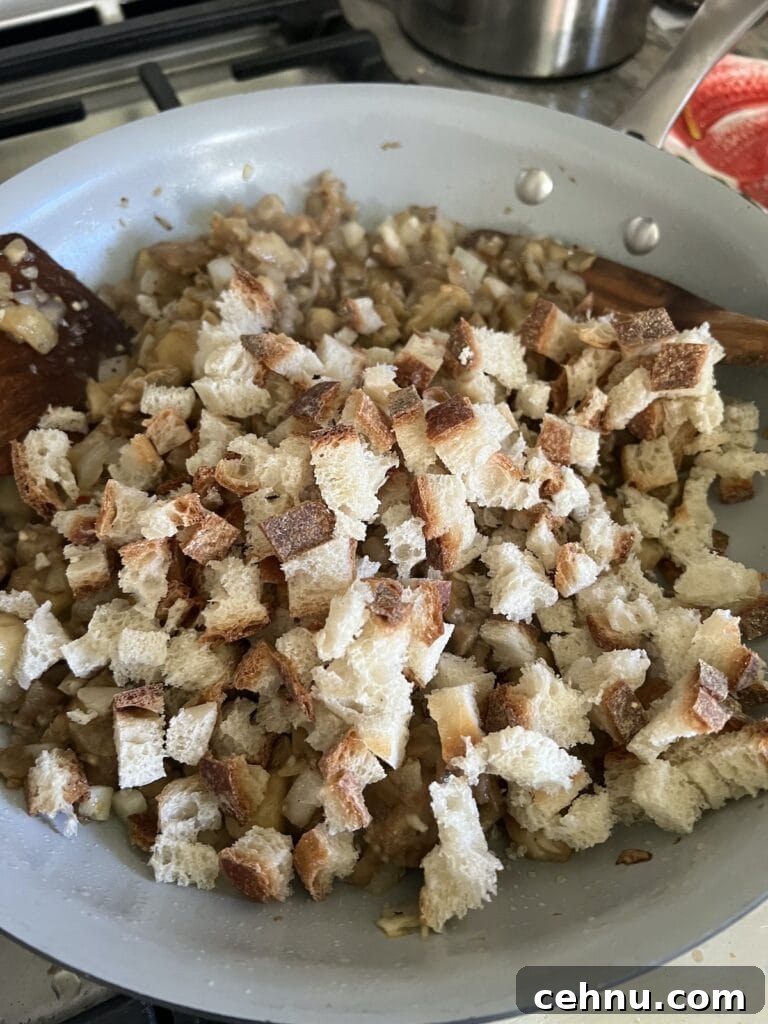 Adding cubed bread to the sautéed eggplant mixture.
