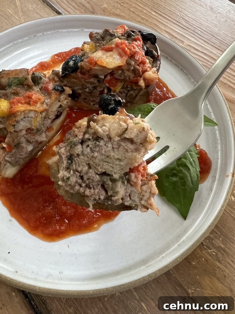Close up of a piece of stuffed eggplant on fork with a plate of it in the background.