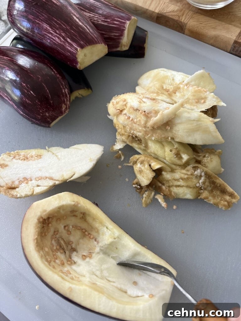 Scraping out the insides of halved eggplant with a spoon.