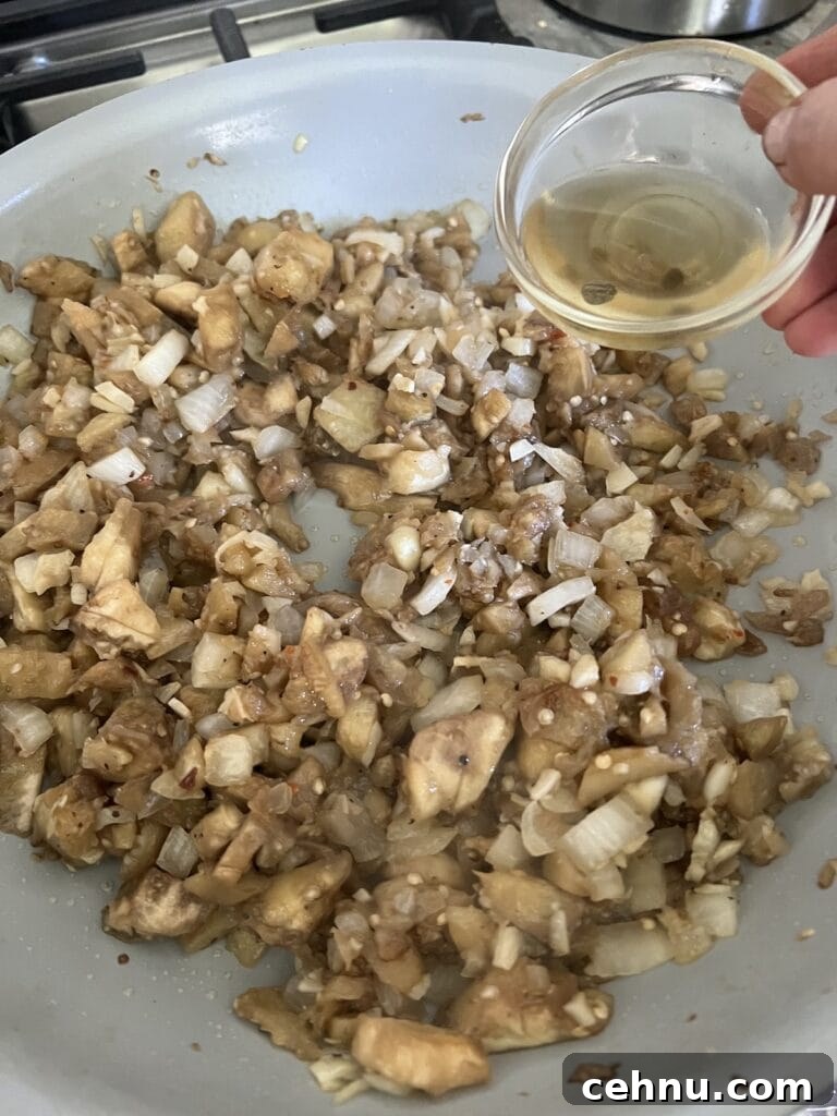 Sauteing the chopped eggplant pulp in pan with onion and adding some wine to it.