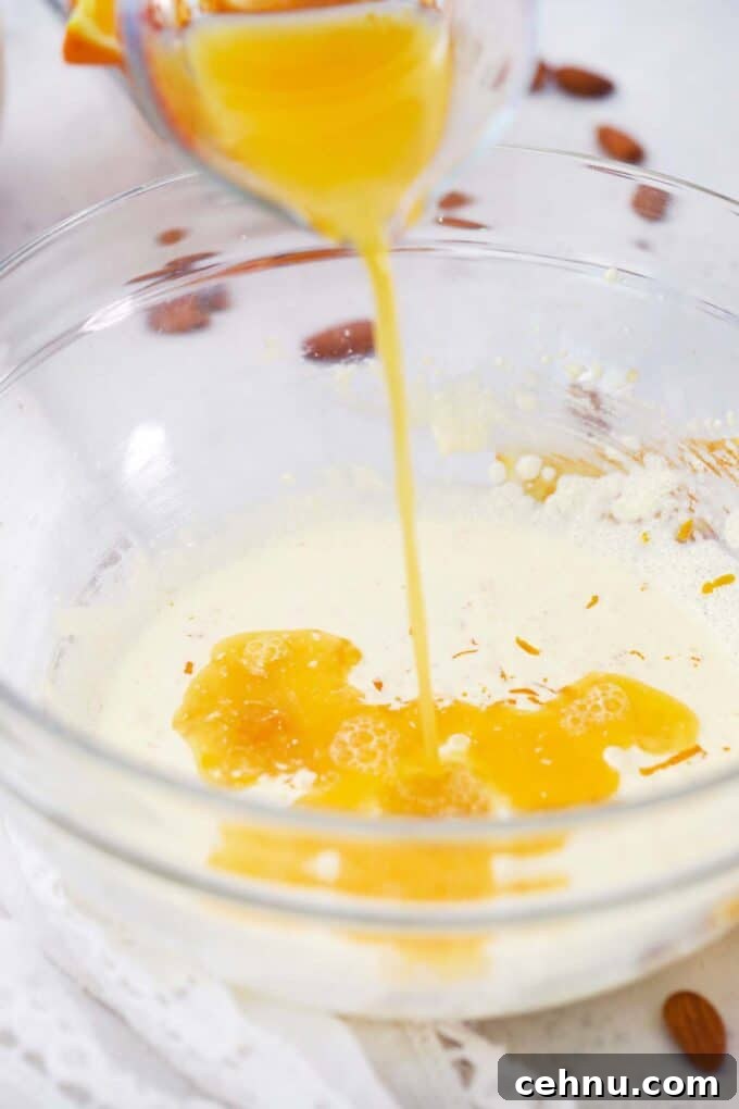 pouring fresh orange juice into cake batter in a bowl