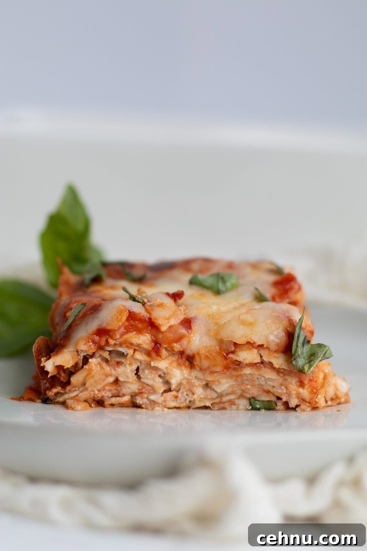 5-Ingredient Matzo Lasagna for Passover Dinner 9 piece of matzo lasagna on a white plate with fresh basil