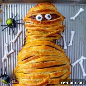 Halloween Mummy Meatloaf Recipe 19 A mummy meatloaf wrapped in pastry with visible eyes on a baking tray.
