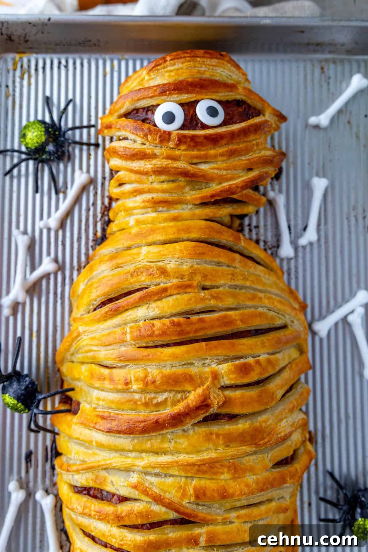 Halloween Mummy Meatloaf Recipe 3 A baked mummy meatloaf wrapped in pastry with googly eyes on a baking sheet.