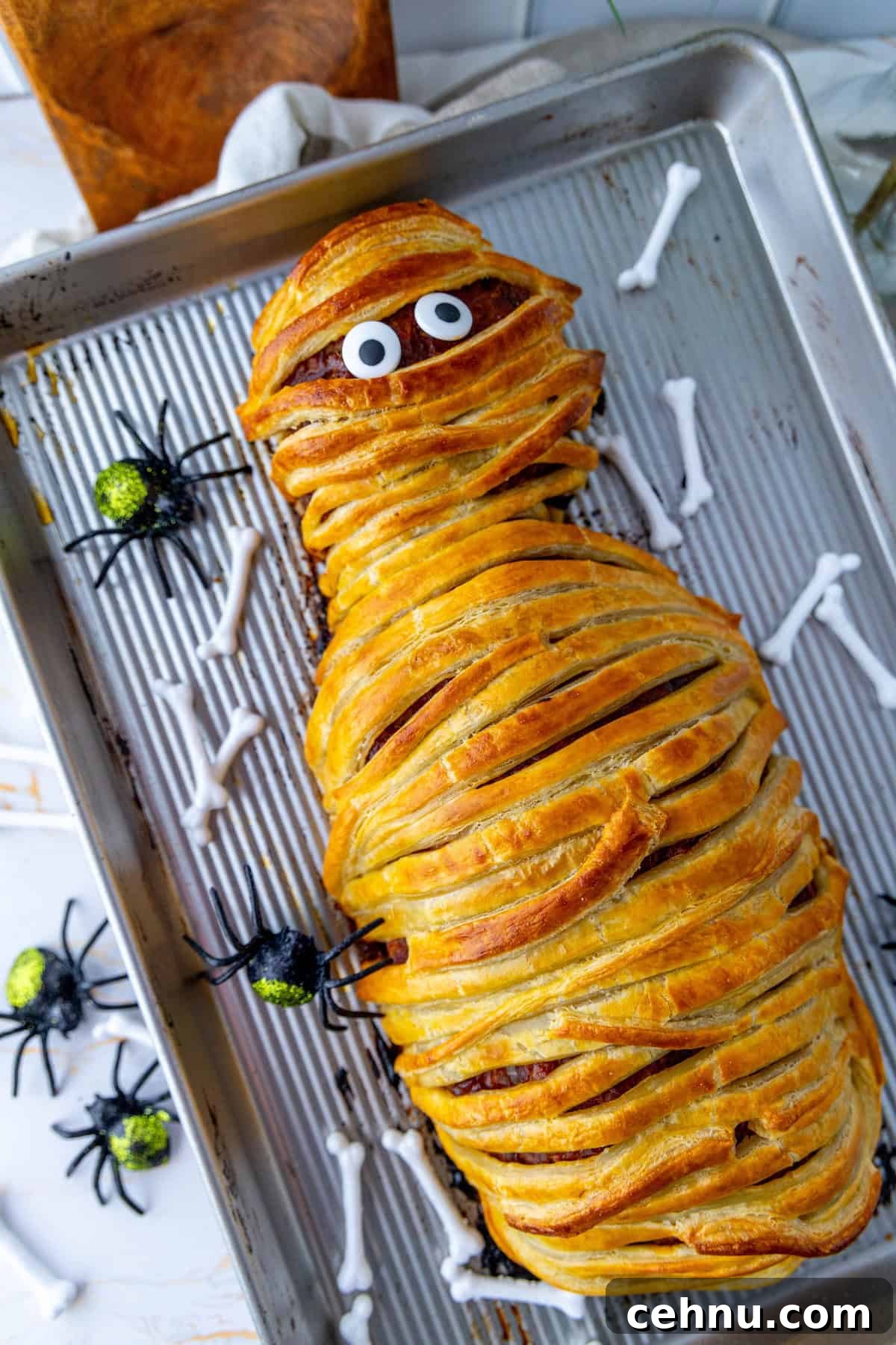 Halloween Mummy Meatloaf Recipe 4 A playful mummy meatloaf with googly eyes on a baking tray with Halloween decorations.