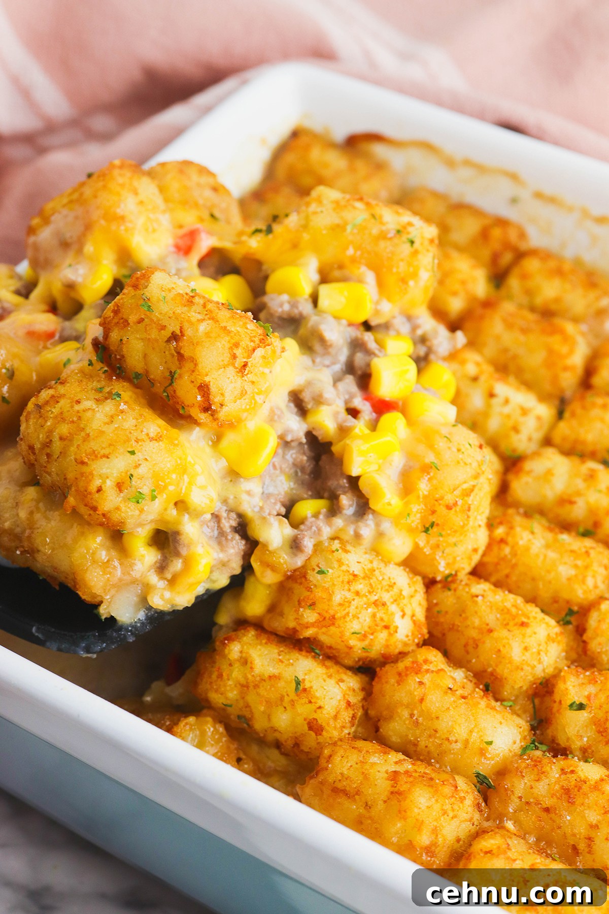 Cheesy Tater Tot Casserole with Ground Beef Recipe 3 A serving spoon full of Tater Tot Casserole held over baking dish.