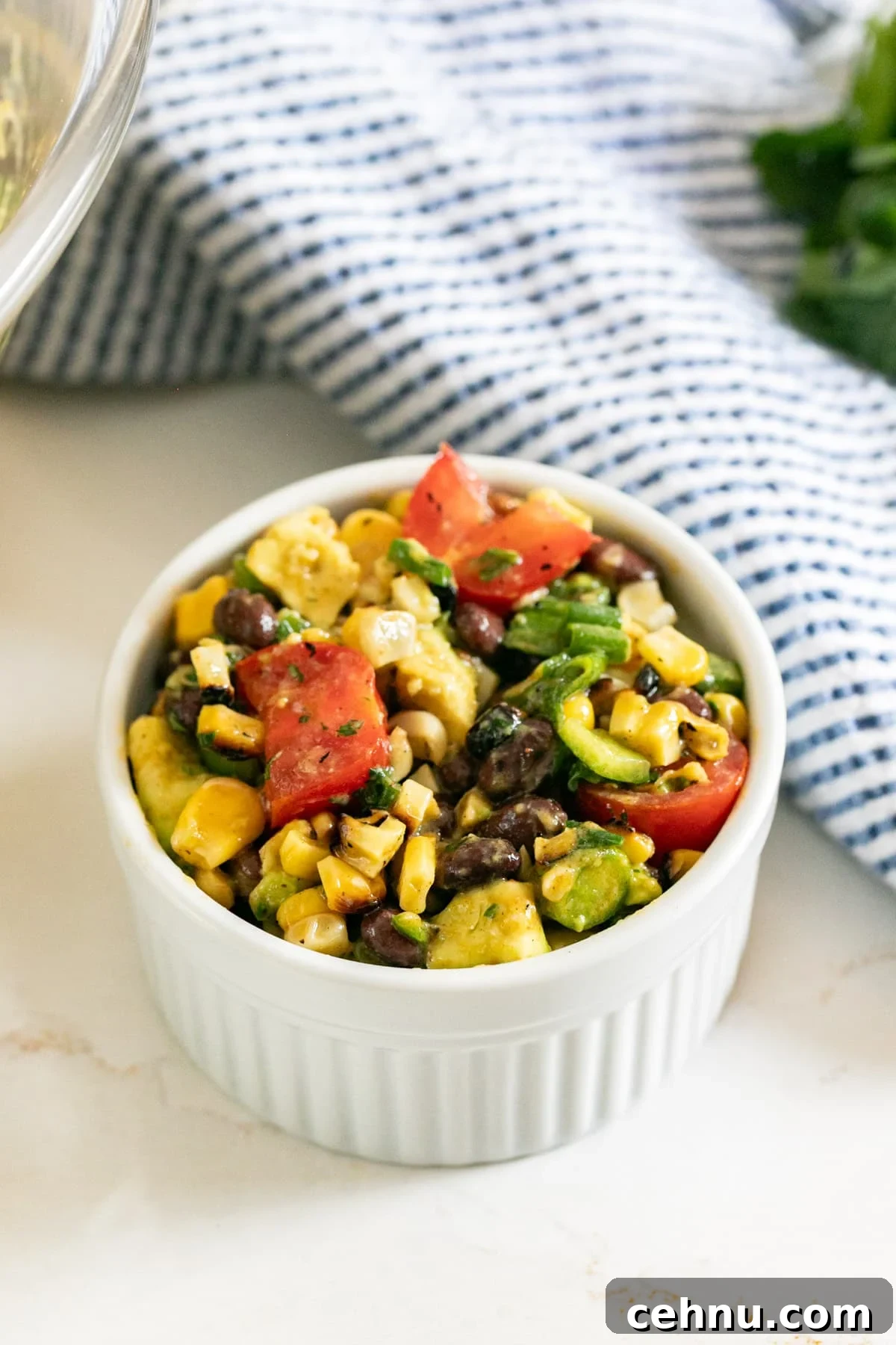 A white bowl of corn salad with a striped napkin behind it.