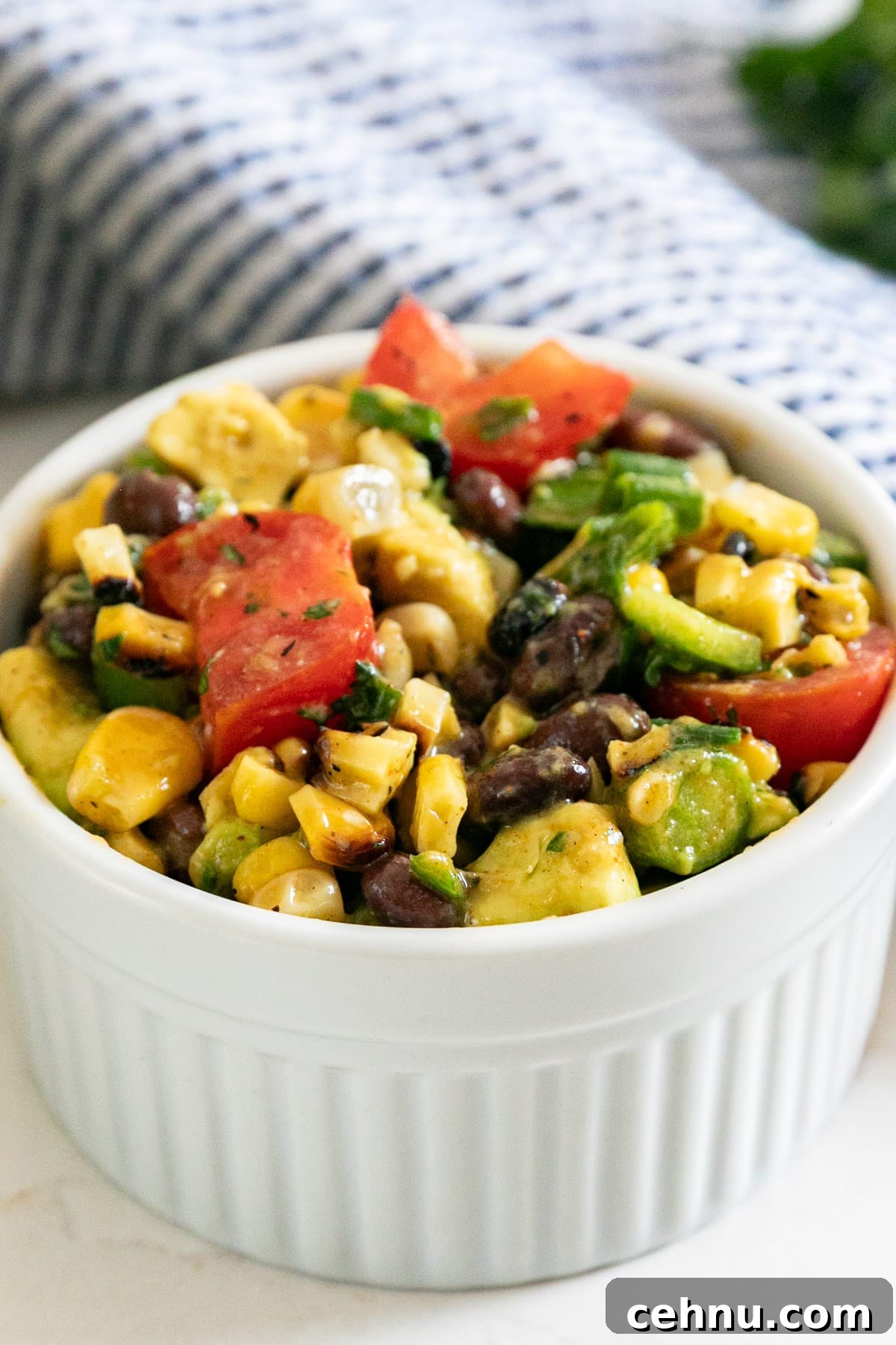 A close up image of a black bean and corn salad in white bowl with a striped napkin behind it.