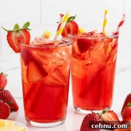 Two tall glasses of strawberry sweet tea with garnishes of fresh lemon and strawberries.