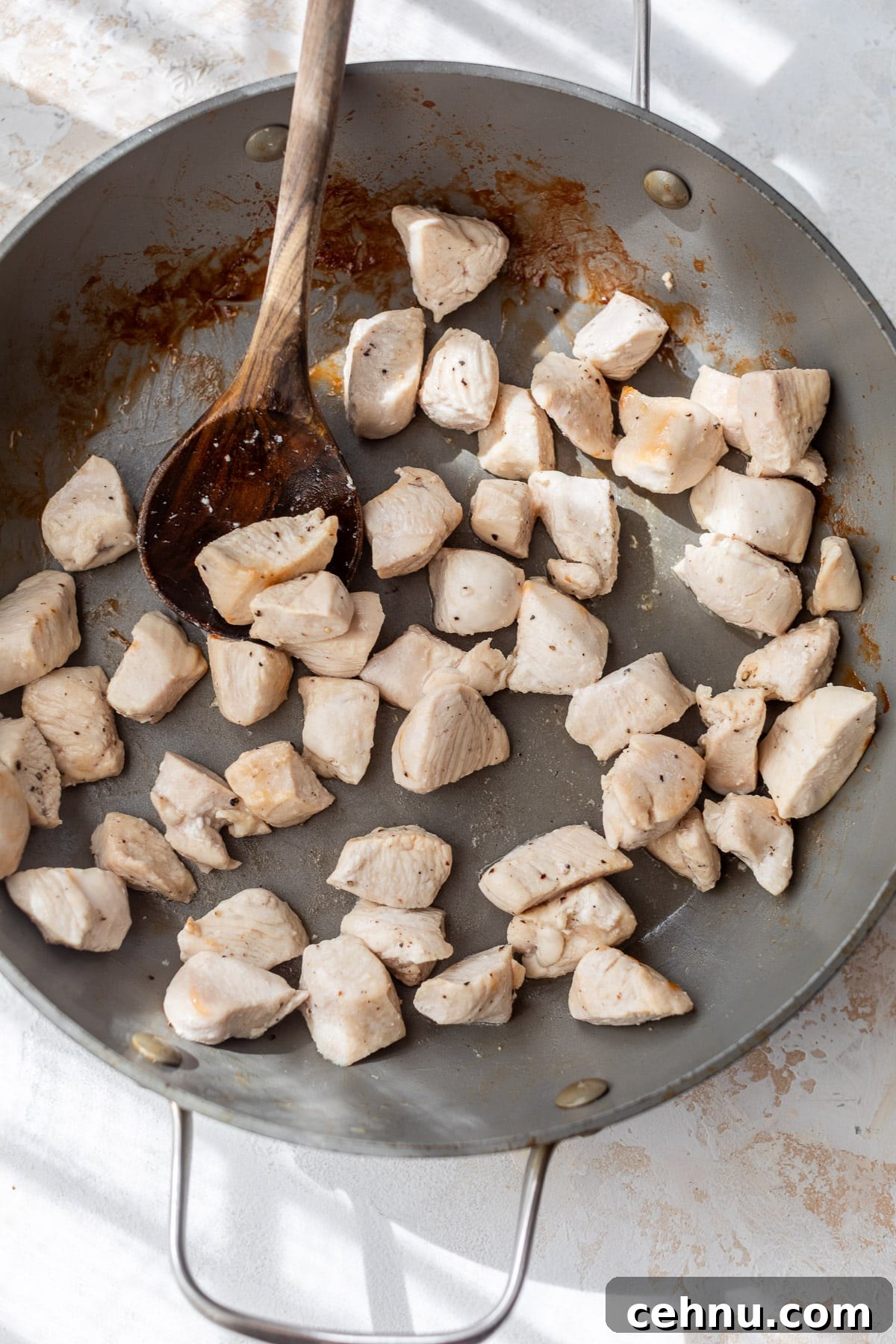 using a wooden spoon to stir cooked chicken bites in a large skillet.