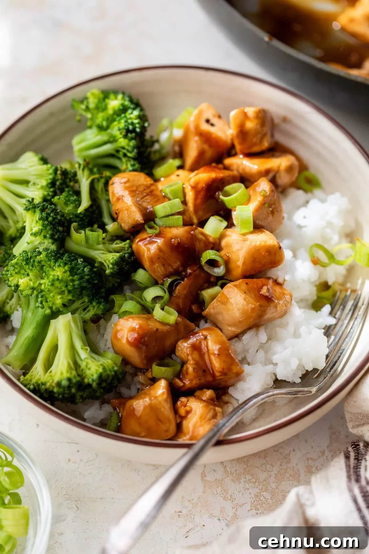 teriyaki chicken and broccoli served over white rice in a bowl.
