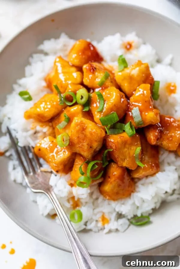 a scoop of saucy orange firecracker chicken served over white rice in a bowl.