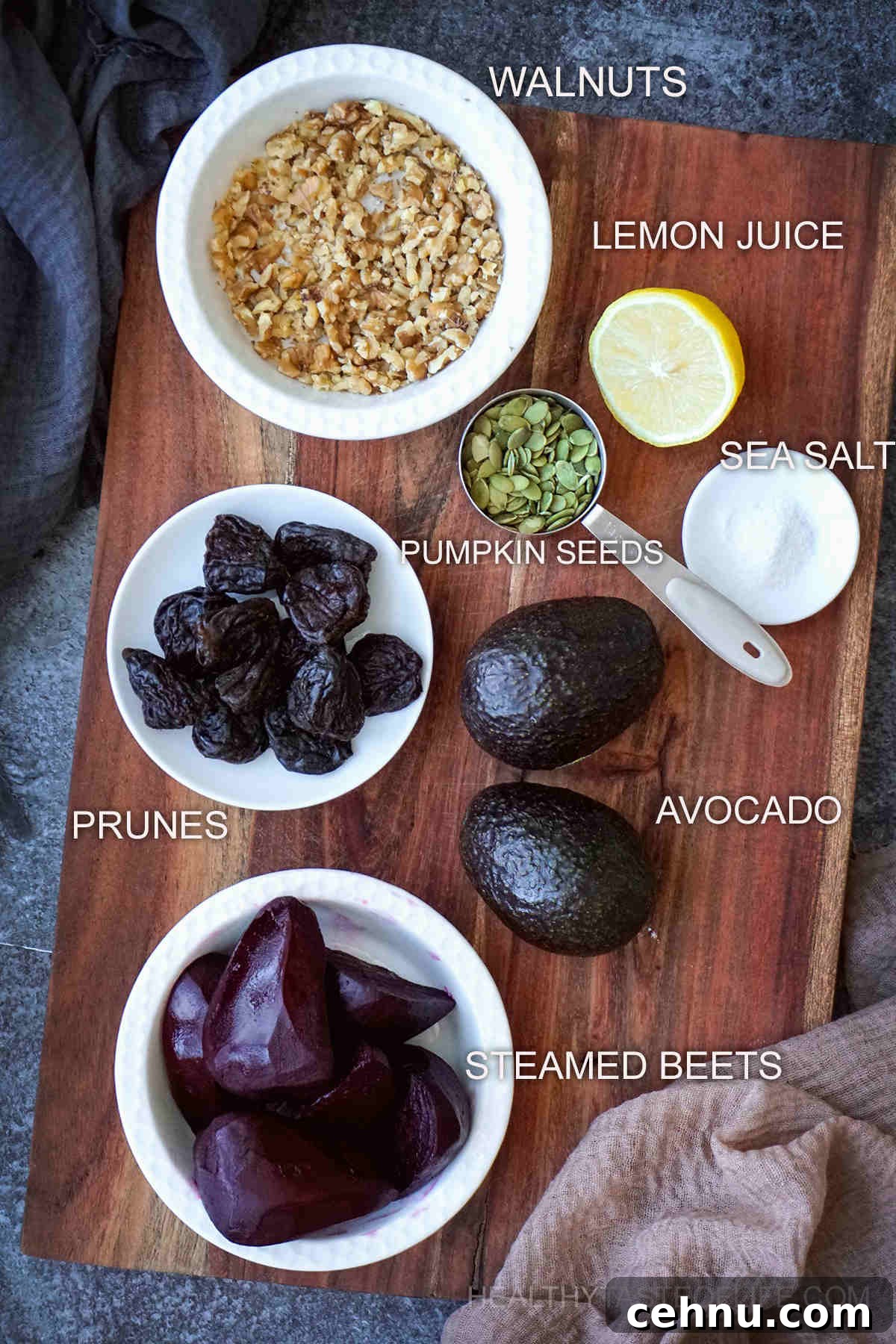 Ingredients for a vegan beet salad displayed on a board: steamed beets, crushed walnuts, avocado, prunes, pumpkin seeds, lemon and salt.