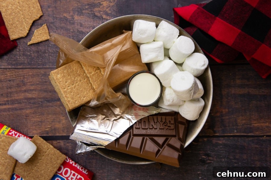 Oven S'mores Dip with Toasted Marshmallows 4 an open chocolate bar, marshmallows, and an open sleeve of graham crackers in a steel pan with a shot glass of cream