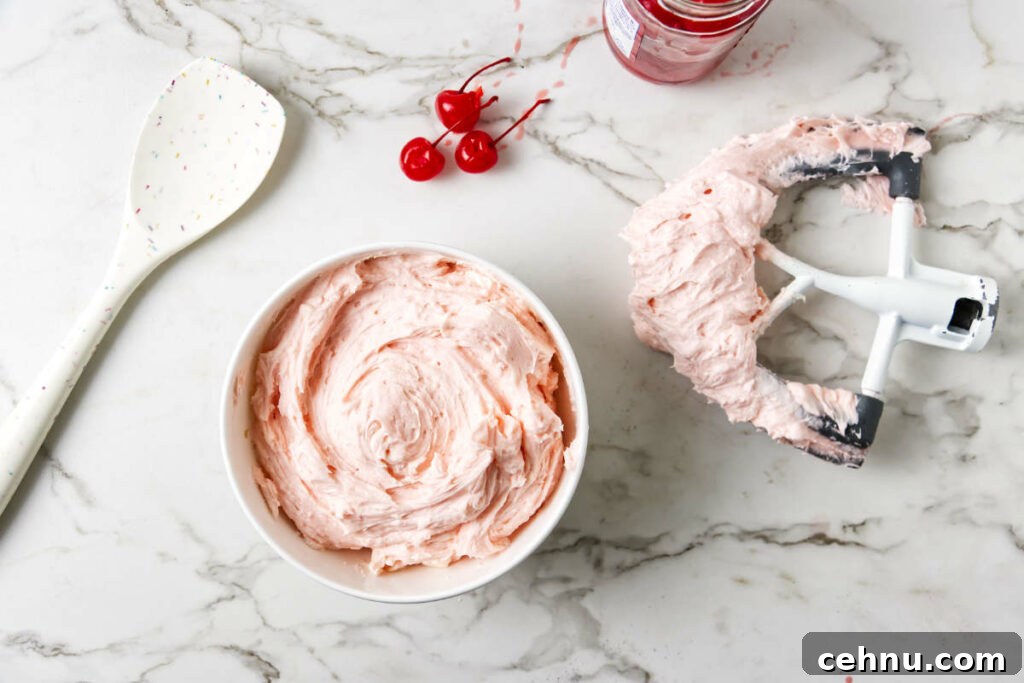 A bowl filled with cherry frosting and a beater next to the bowl.
