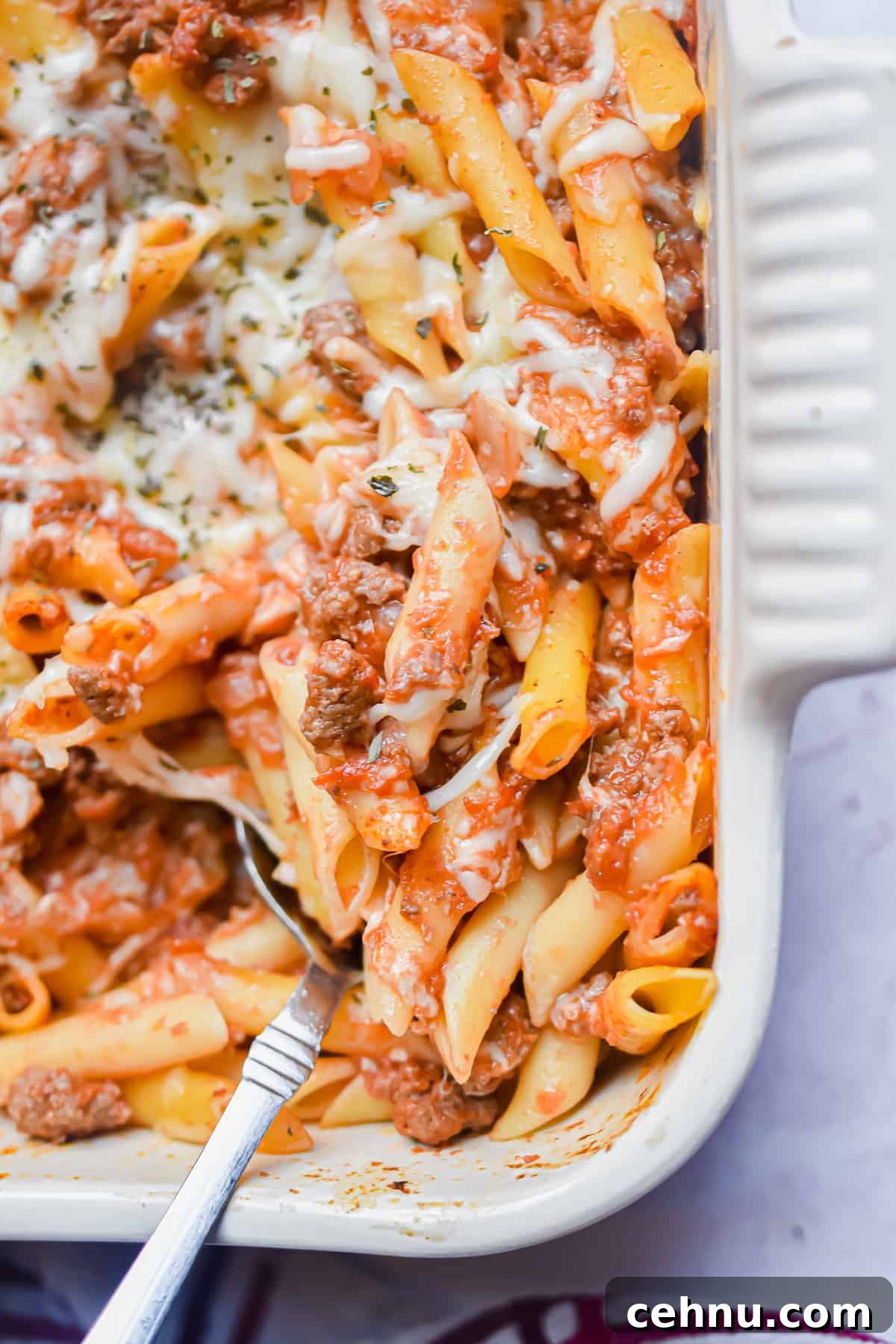 A spoon is in the baking dish with the meaty marinara pasta bake.
