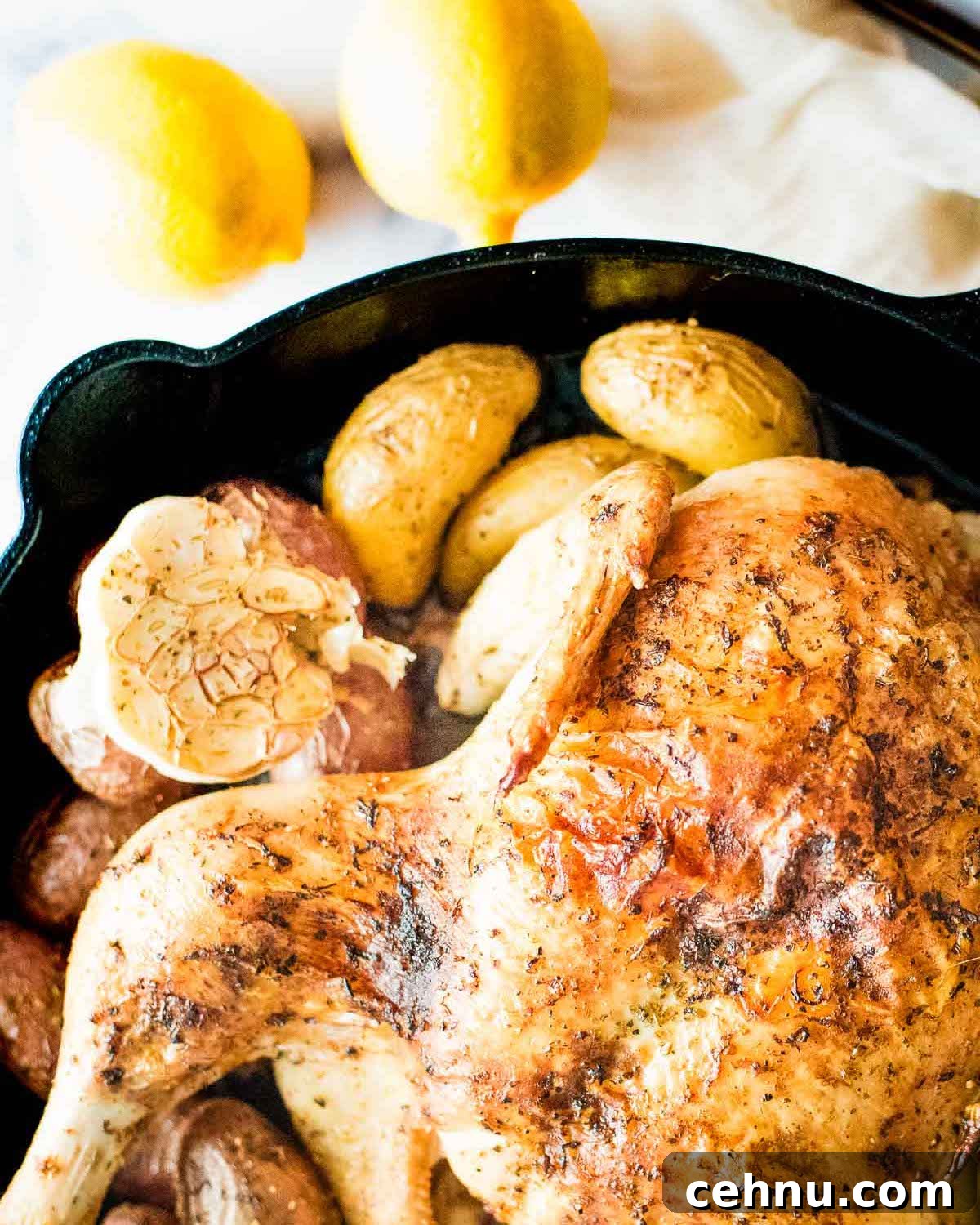 A chicken in a cast iron skillet with potatoes and lemons.