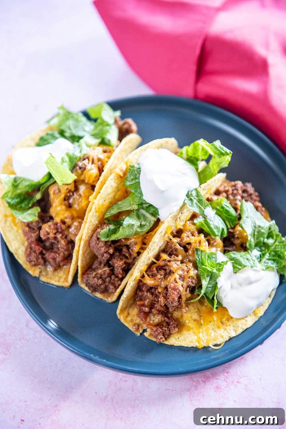 Slow Cooker Taco Meat Recipe: Tender, Flavorful Filling 2 3 beef tacos garnished with cheese, parsley, and sour cream served on a blue plate