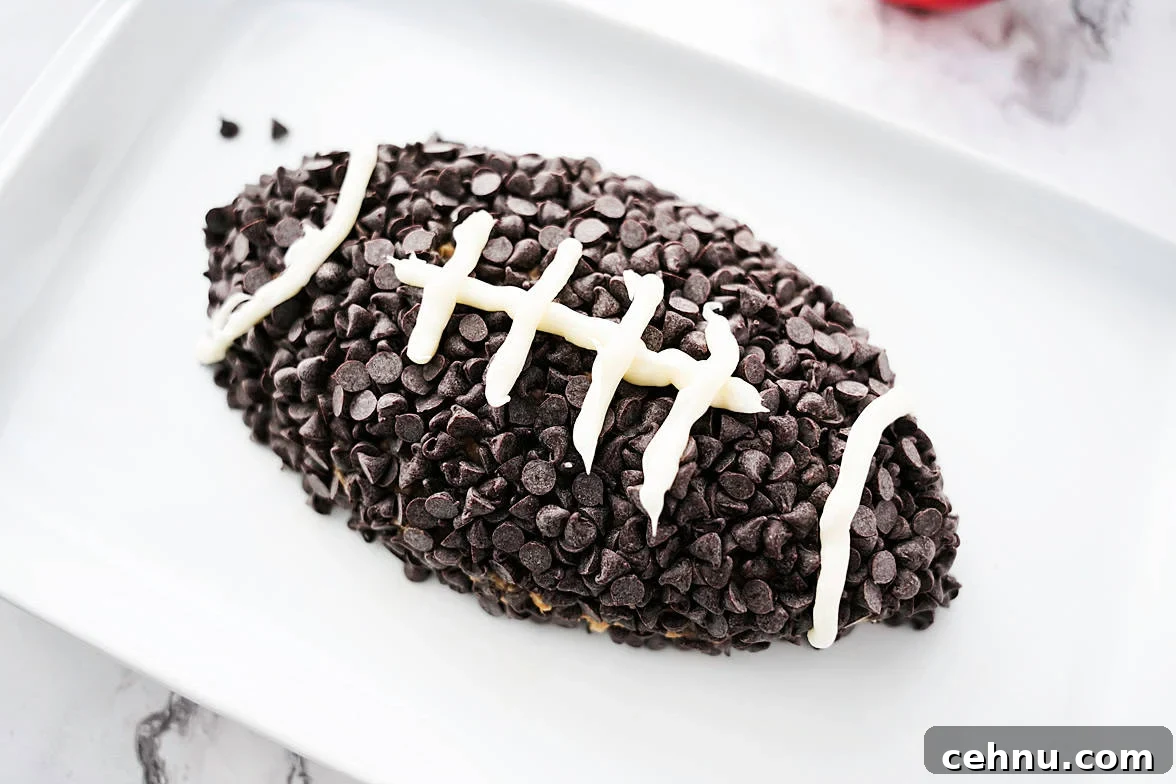 white serving platter with apple toffee dip after being shaped into a football, topped with mini morsels and white icing for laces of the football