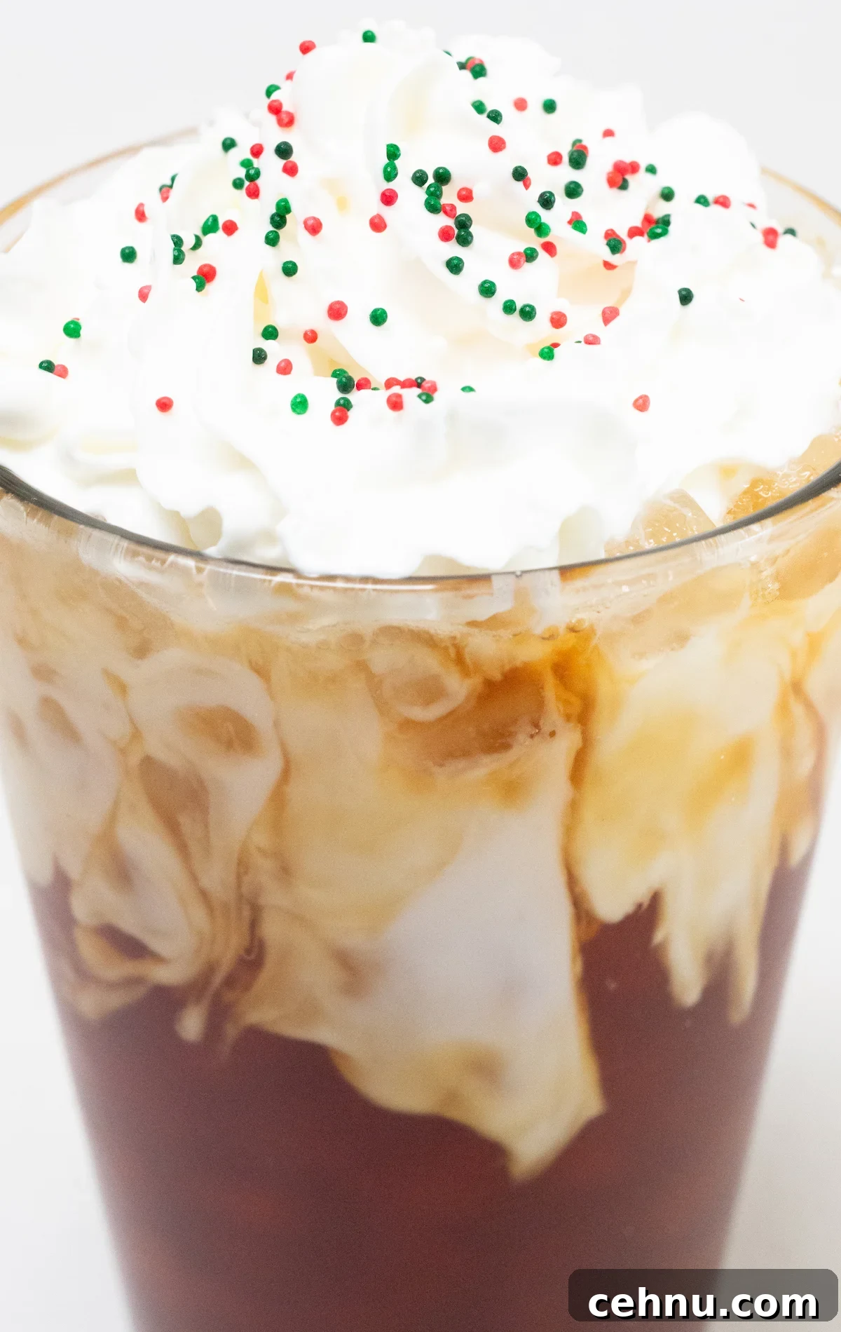 Close up of a pint glass that's filled with coffee and almond milk then topped with whipped cream and red, white, and green Christmas sprinkles.