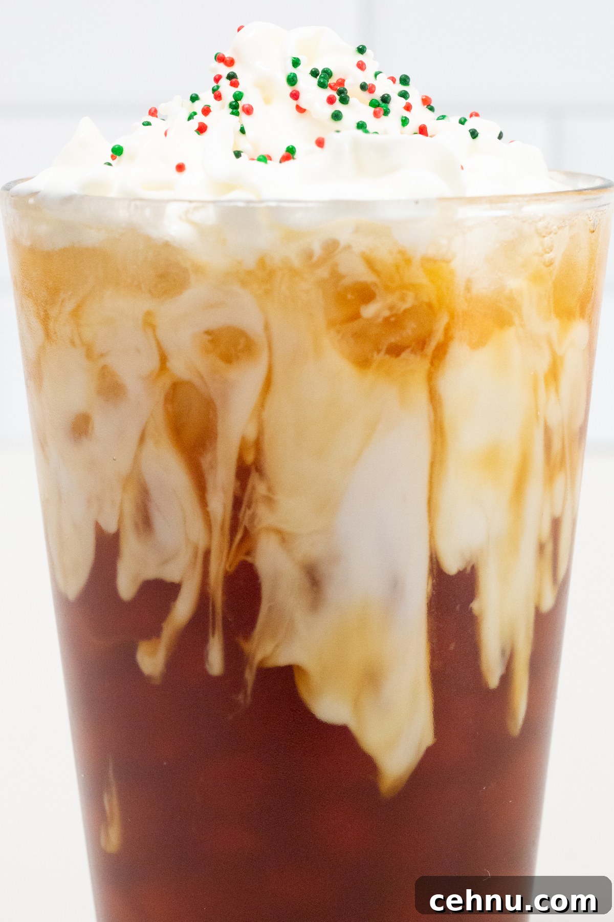 A medium shot of a pint glass. The bottom is filled with espresso, the top has almond milk and whipped cream with red, green, and white Christmas sprinkles.