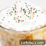 Close up of a pint glass that's filled with coffee and almond milk then topped with whipped cream and red, white, and green Christmas sprinkles.