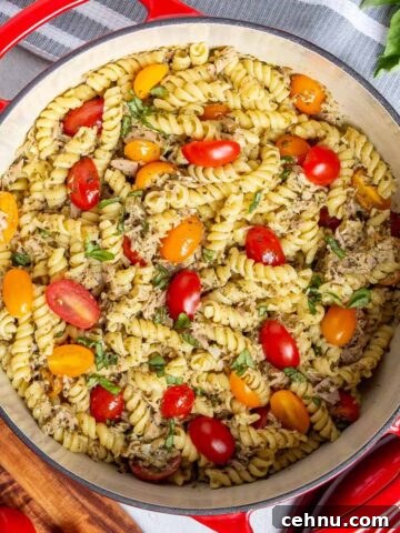 Tuna pesto pasta in a 6-quart dutch oven garnished with fresh basil. Halved cherry tomatoes are mixed in.