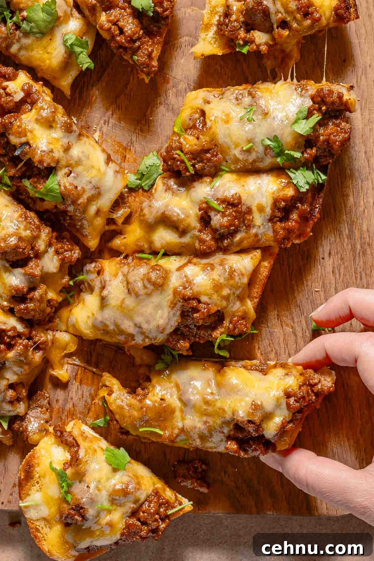 Garlic Bread Sloppy Joes Recipe for Cheesy Saucy Sandwiches 10 hand pulling slice of garlic bread from cut loaf covered with sloppy joe meat and cheese.