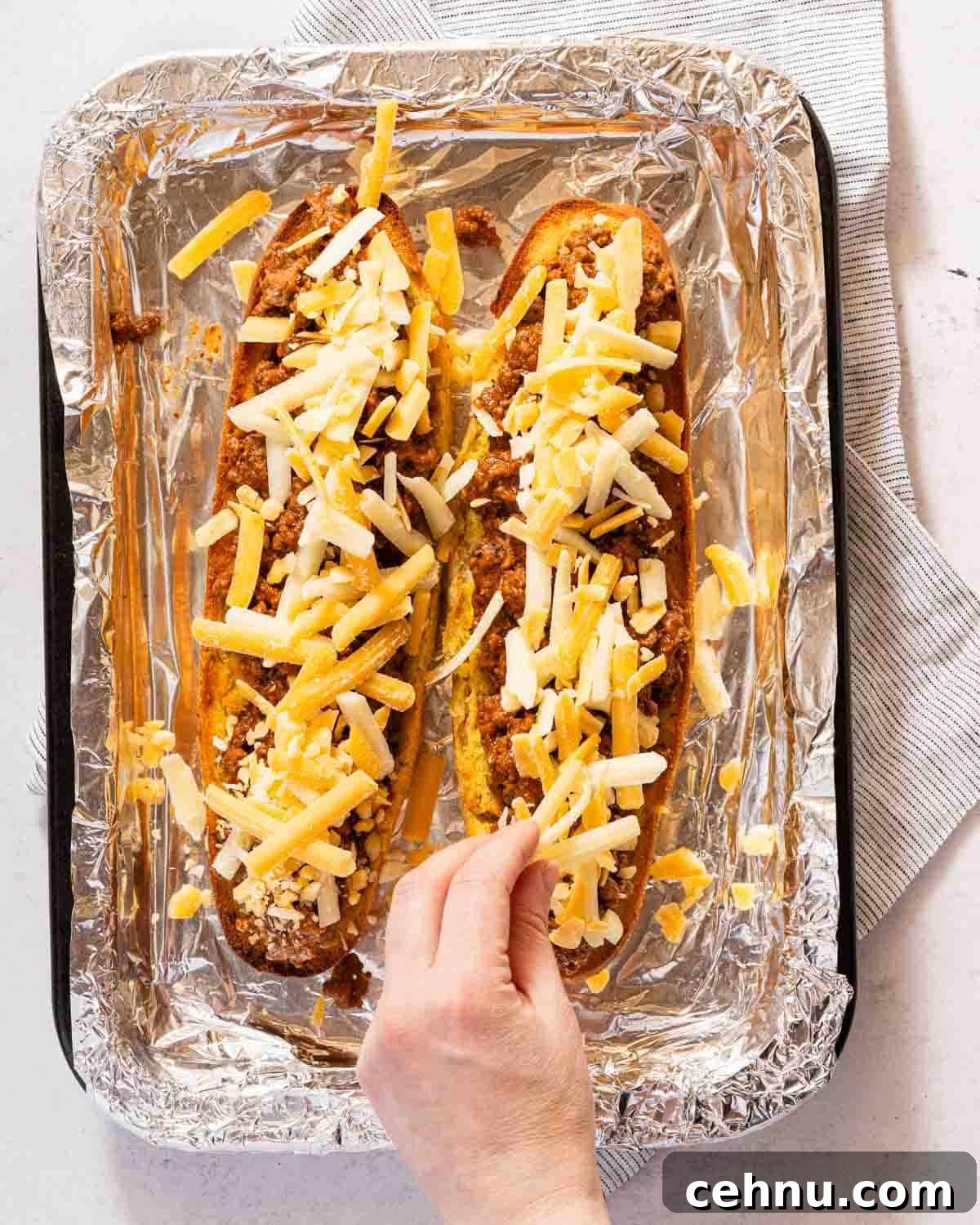 Garlic Bread Sloppy Joes Recipe for Cheesy Saucy Sandwiches 9 hand sprinkling shredded cheese on garlic bread topped with sloppy joe meat.