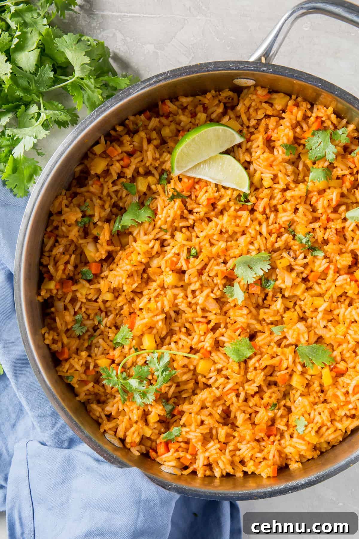 Authentic Restaurant-Style Mexican Rice Recipe 2 A skillet filled with Mexican rice, cilantro and slices of lime.
