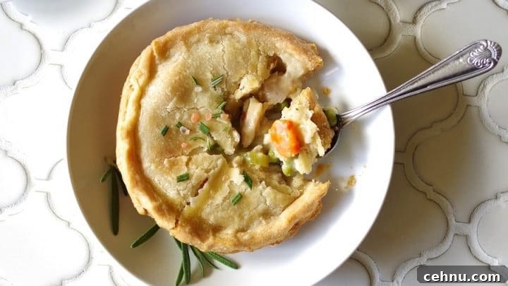 A close up of a Gluten-Free Chicken Pot Pie topped with salt and rosemary on a white plate, with a spoon taking a bite out