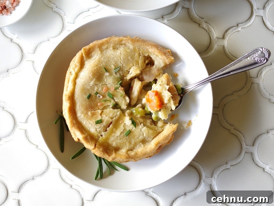 Gluten Free Chicken Pot Pie Recipe with Flaky Crust 6 a top down view of a Gluten-Free Chicken Pot Pie topped with salt and rosemary on a white plate, with a spoon taking a bite out