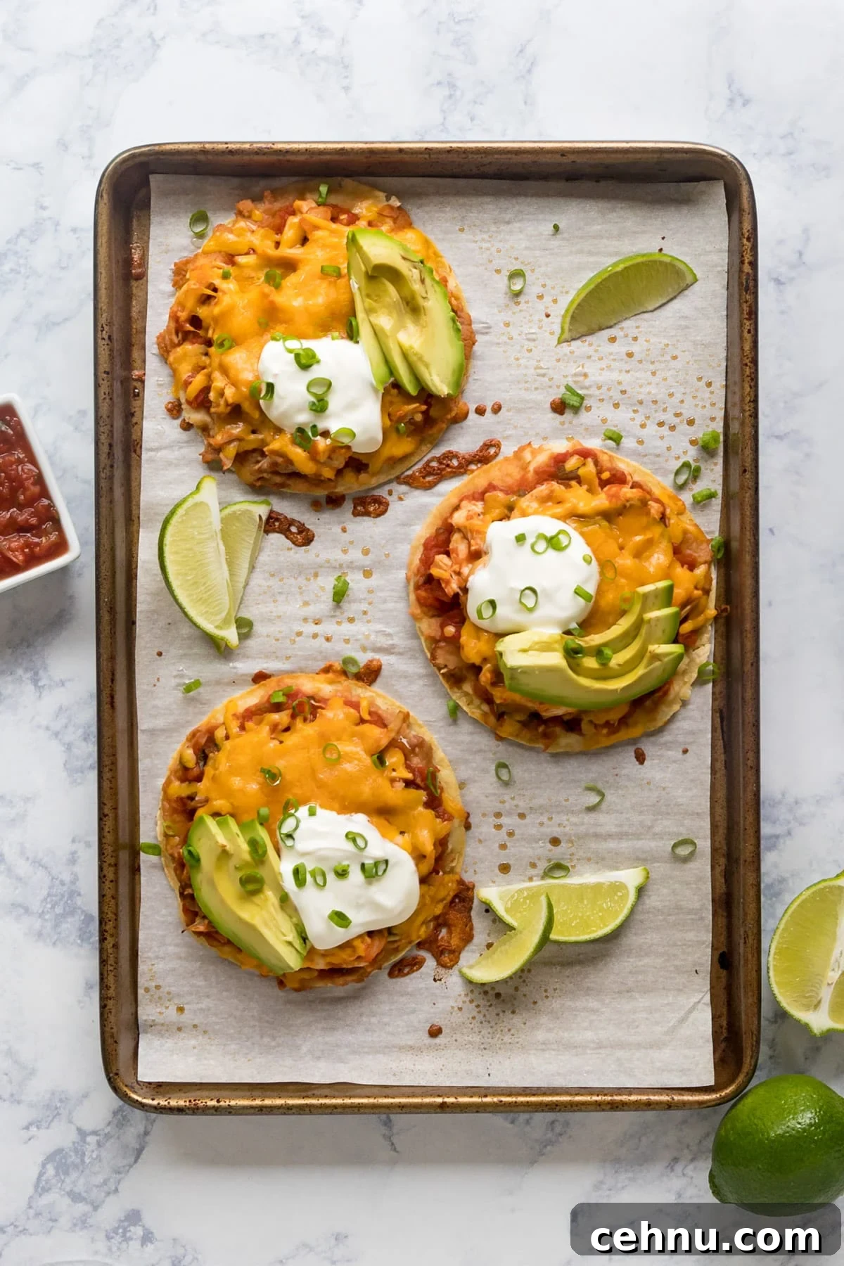 An overhead image of a pan with 3 tostadas on it with limes and avocado.