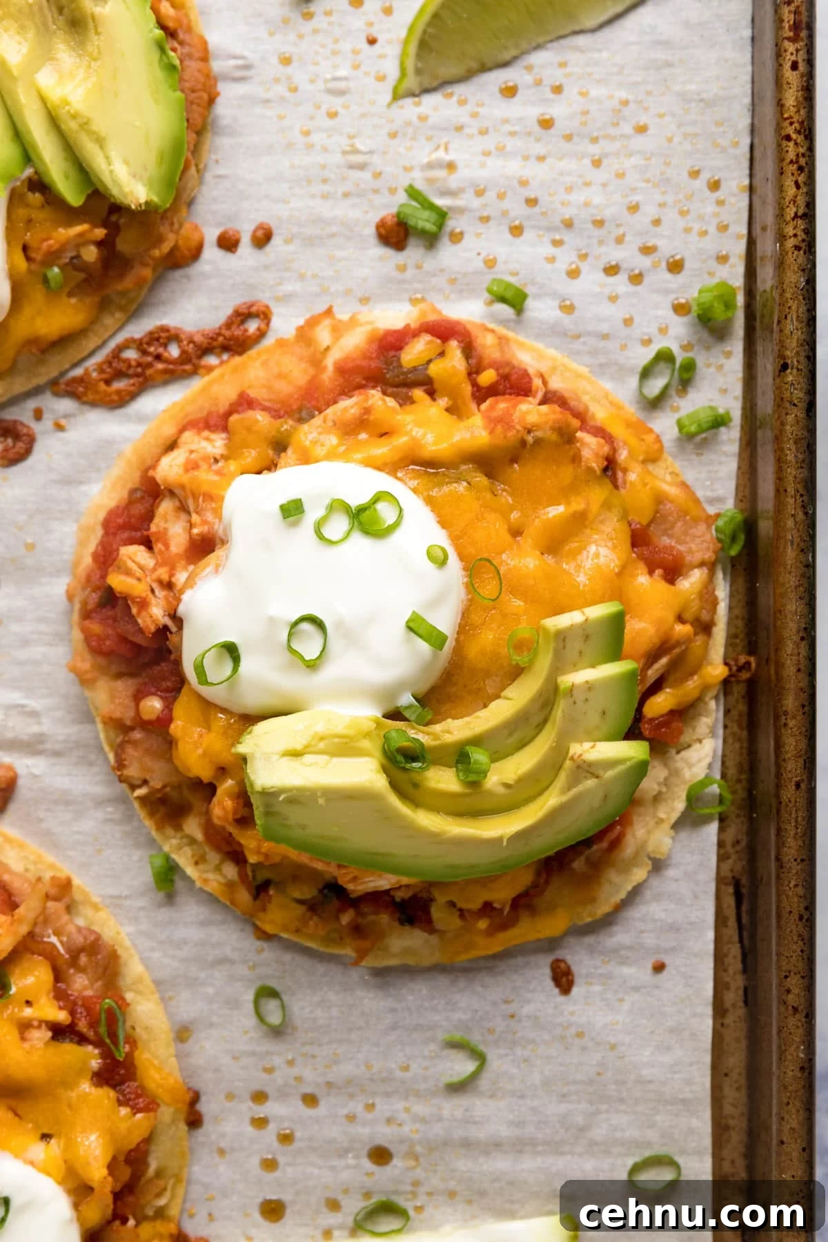 An overhead image of a chicken tostada on the pan with sour cream and avocado on top.