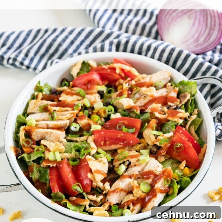 A bowl of BBQ chicken salad with a striped napkin, half red onion and fried onions around it.