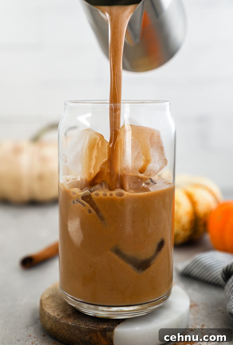 A blended pumpkin spice latte being poured over a glass of ice