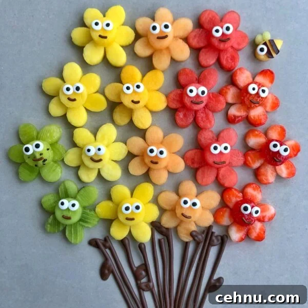 An arrangement of colorful fruit slices shaped like flowers with cartoon faces and chocolate stems. A mango bee is seen in the background.