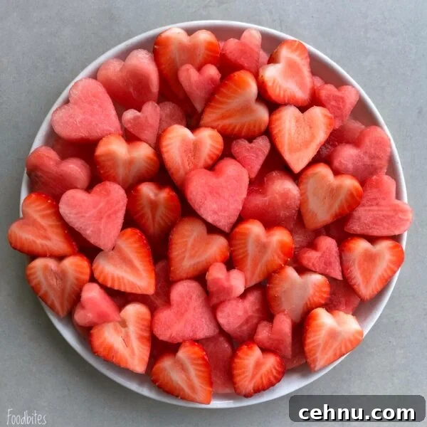 A white plate filled with heart-shaped pieces of watermelon and strawberries on a light gray surface.