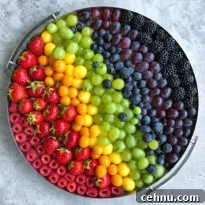 A round tray displays rows of colorful fruits arranged in a rainbow pattern.