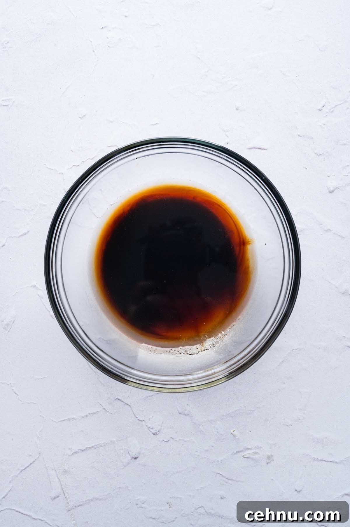 A clear glass bowl containing dark brown Thai basil pork sauce, placed on a textured white surface.