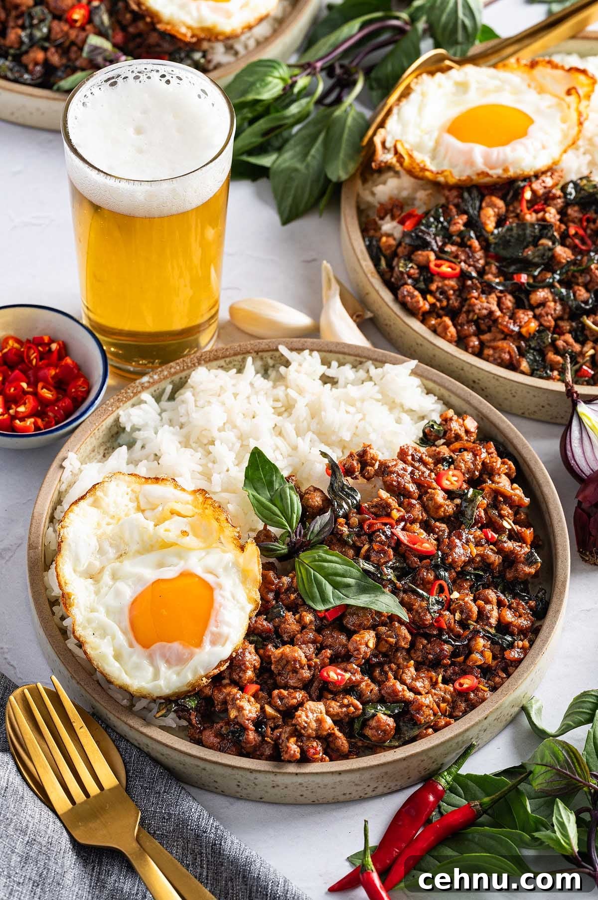 A plate of rice with Thai basil pork, stir-fried to perfection, and topped with a crispy fried egg. It's garnished with red chili for an added kick and best enjoyed alongside a refreshing glass of beer.