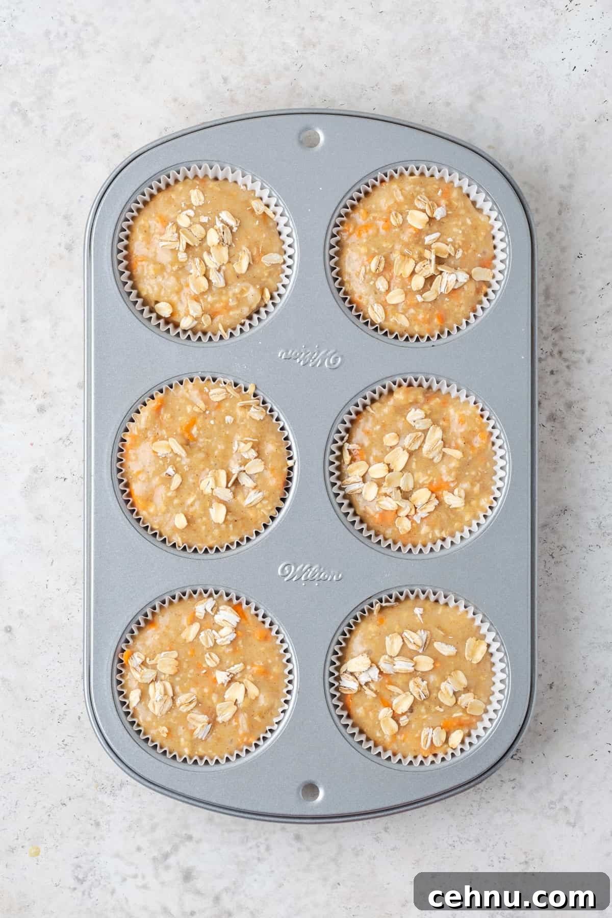 Moist Applesauce Carrot Muffin Recipe with Cinnamon 9 Unbaked applesauce carrot muffin batter topped with a sprinkle of oats in a 6 portion muffin tin.