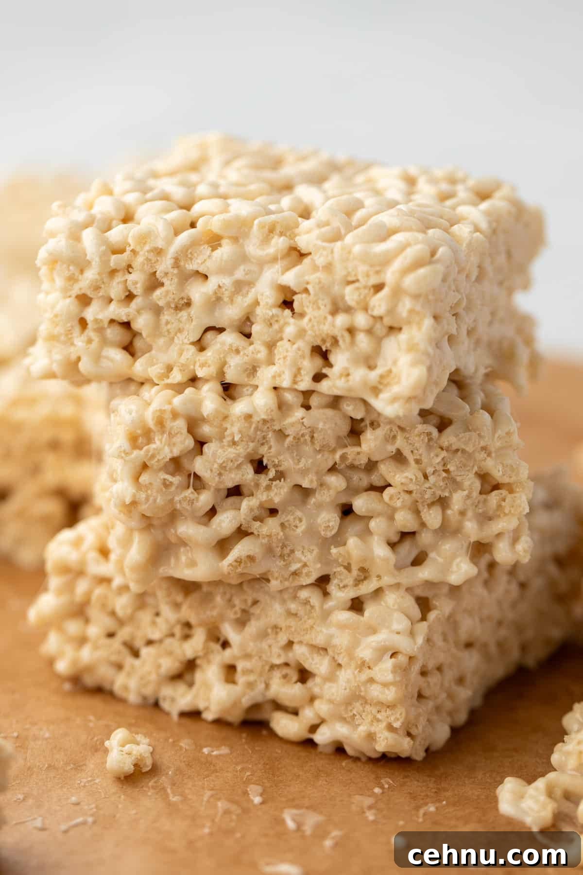 Gluten-Free Rice Krispie Treats Recipe 7 A stack of three rice cereal treats resting on parchment paper.
