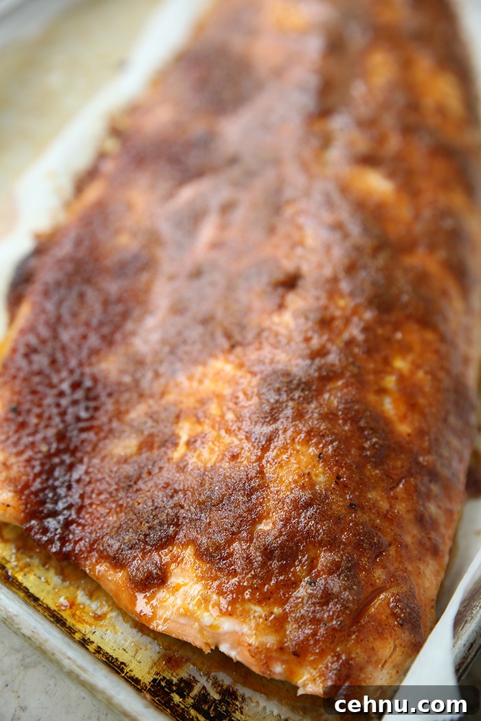 A large filet of sweet and smoky brown sugar salmon sitting on parchment paper on a baking sheet.